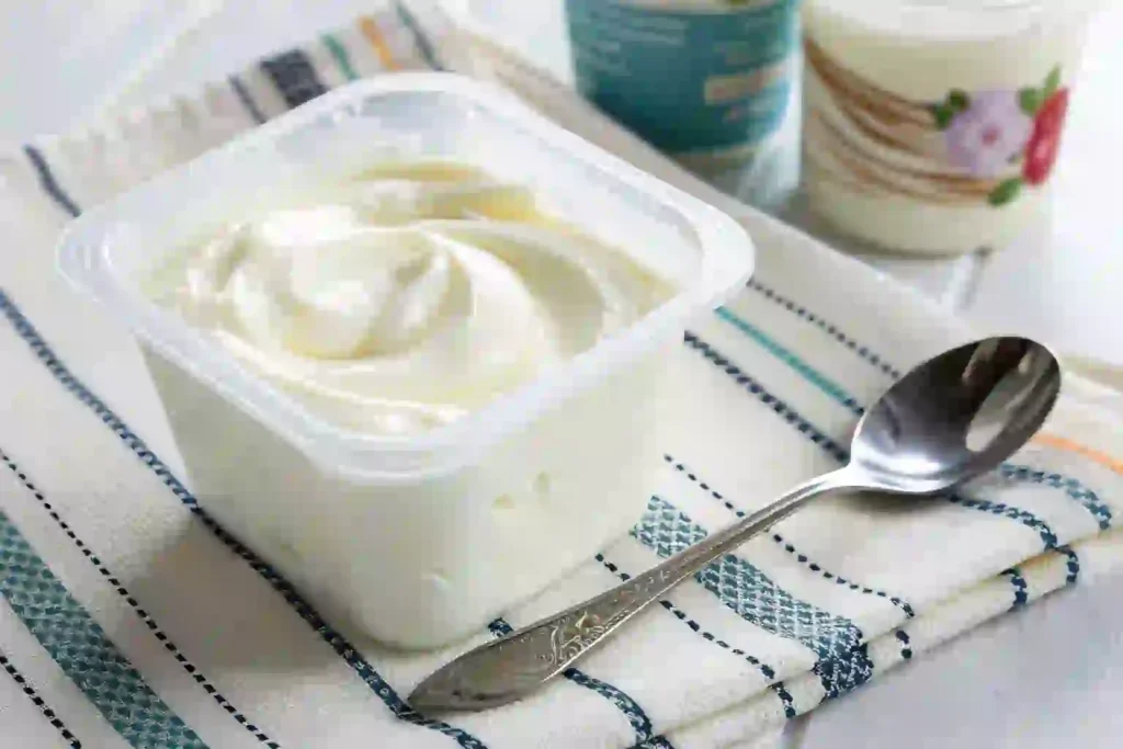 Open tub of plain Greek yogurt with spoon on a dish towel